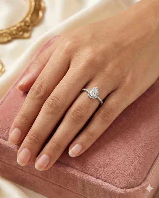 Teardrop White Topaz ring with halo setting and pave silver band on black background.