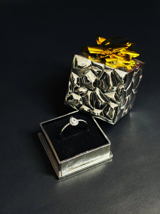 Teardrop White Topaz ring with halo setting and pave silver band on black background.