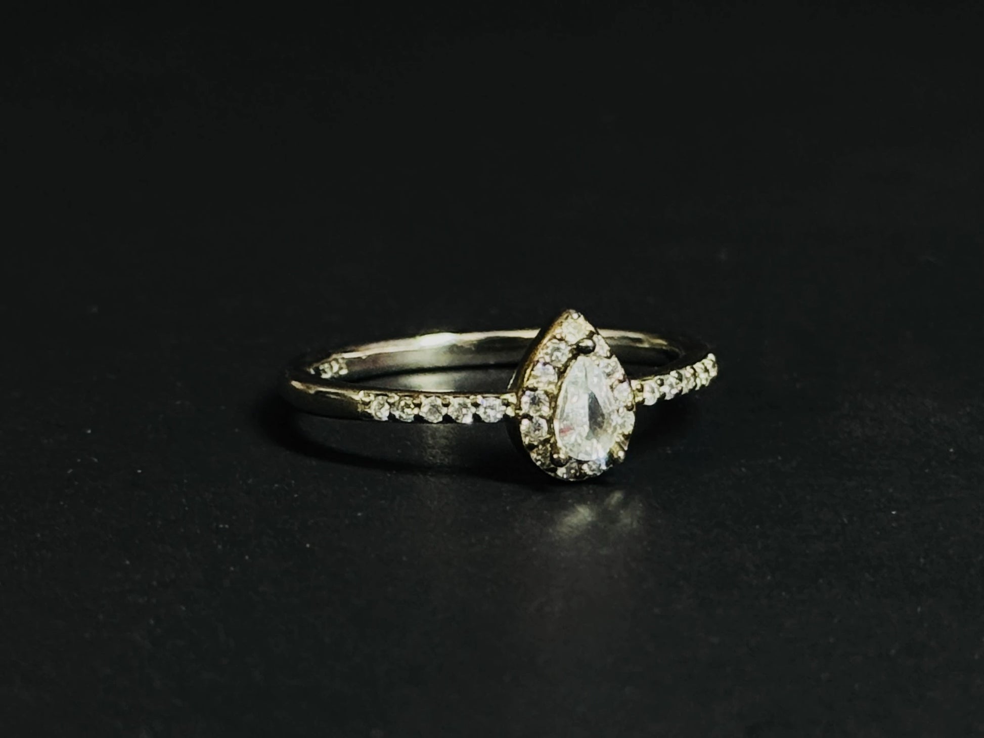 Teardrop White Topaz ring with halo setting and pave silver band on black background.